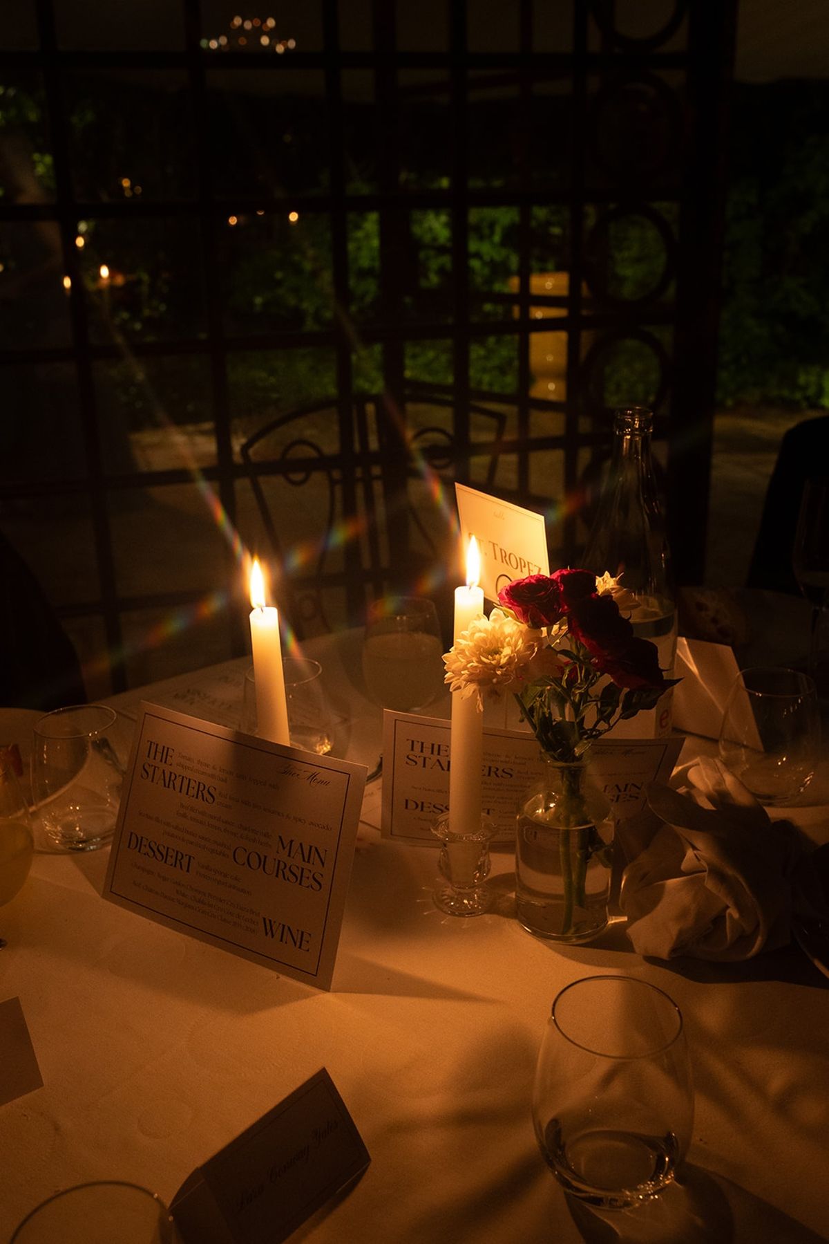 Candlelit table with St Tropez place card, tapers, crimson blooms and folded menus
