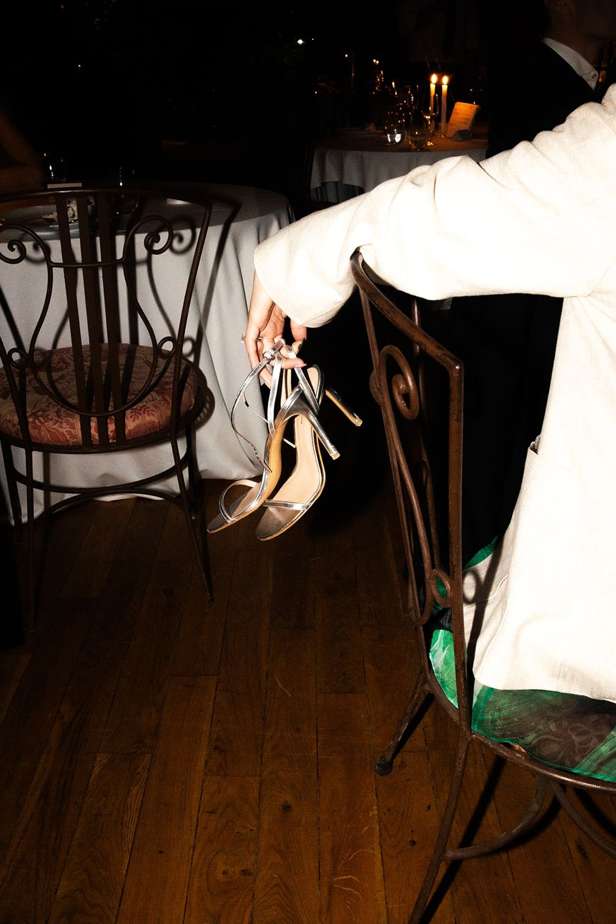 Guest dangles silver strappy heels off wrought iron chair as tables glow in background