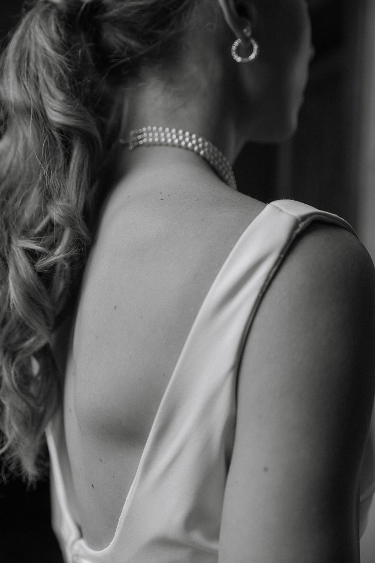 Close detail of bride from behind with triple-strand pearl choker and satin gown back