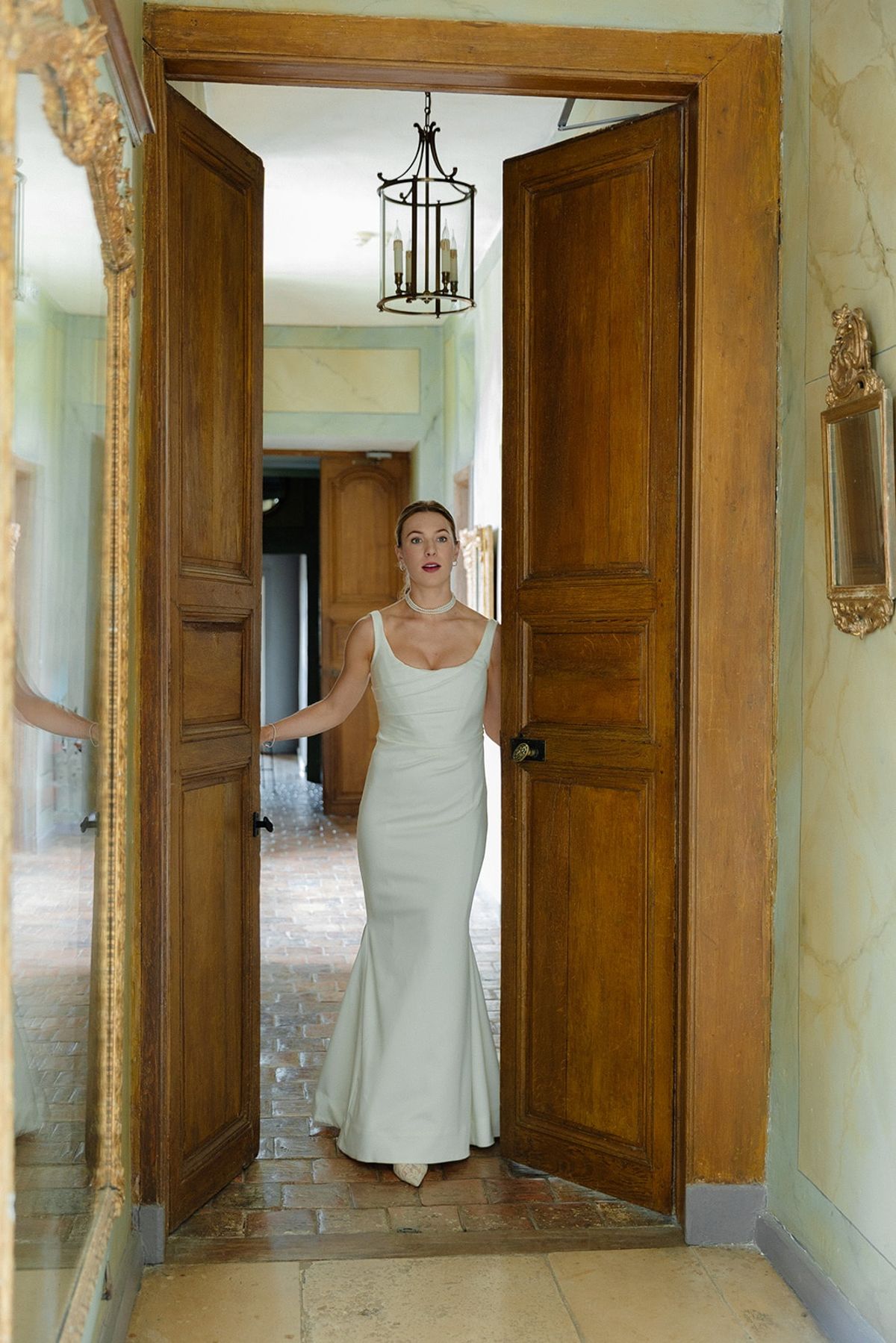 Bride framed by tall wooden double doors under iron lantern over brick floor