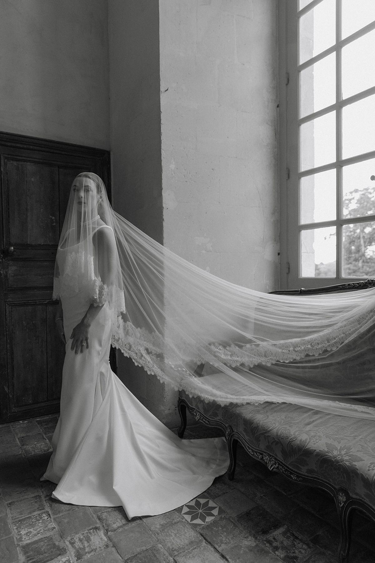 Bride beside antique chaise with veil falling across upholstery in chateau room