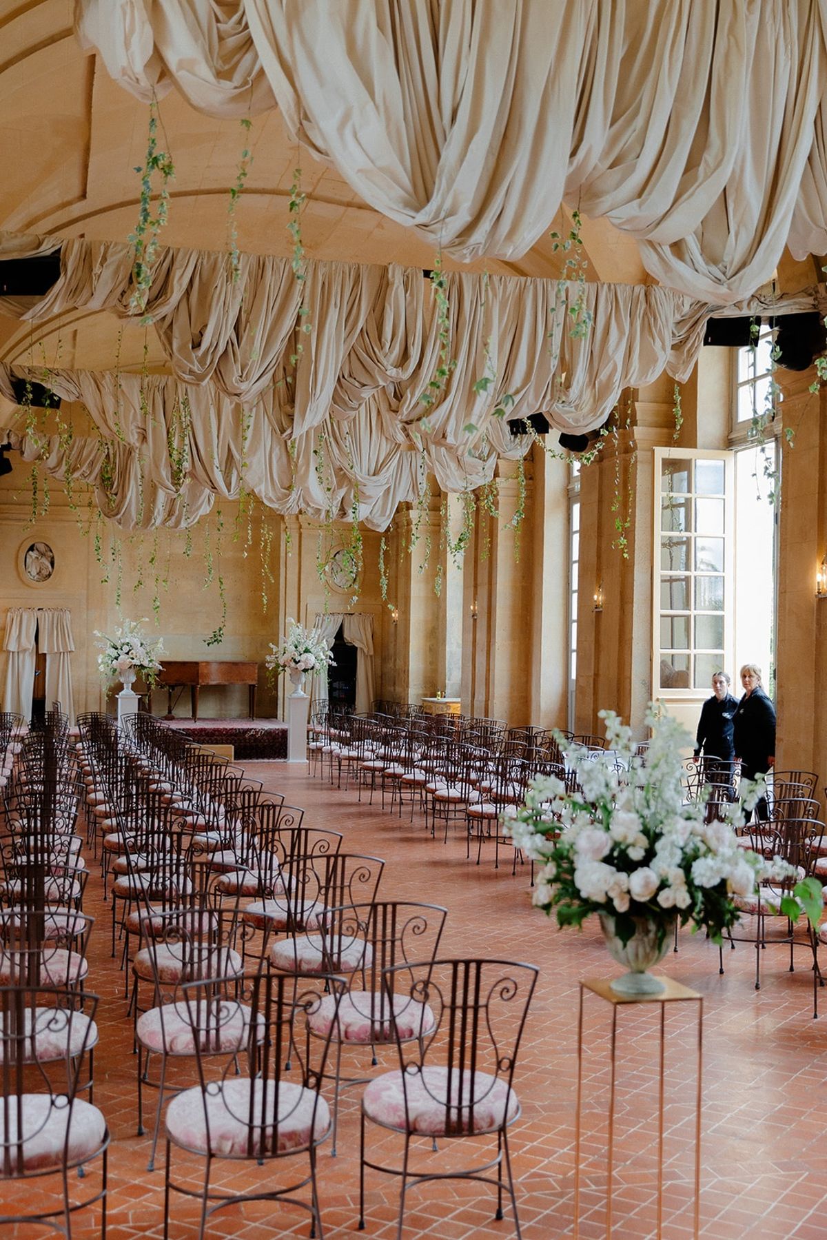 Empty chateau ceremony hall with draped fabric canopy and iron chairs in rows