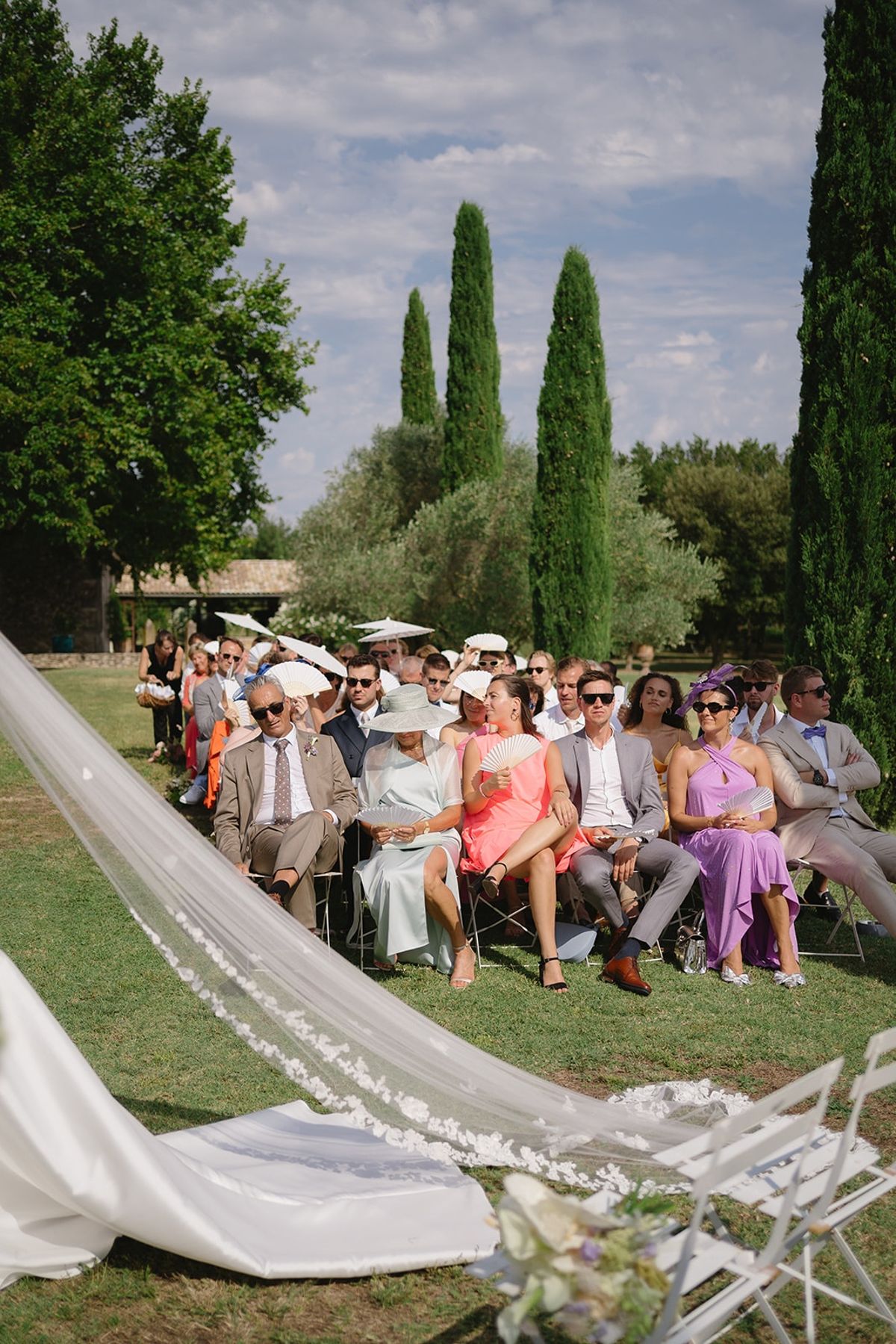 Guests seated at outdoor ceremony with bride's veil trailing at Les Domaines de Patras, Provence