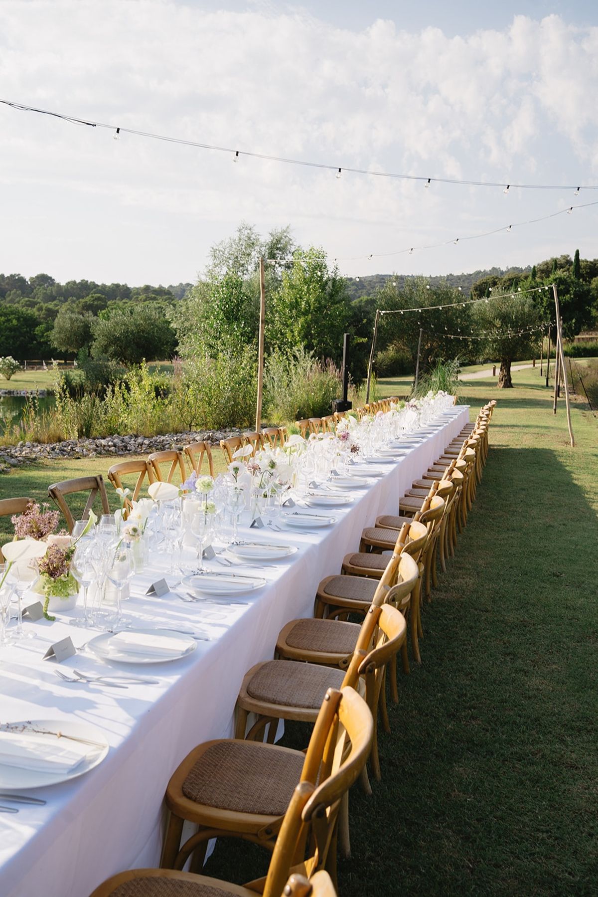 Empty long banquet table with cross-back chairs and string lights at Les Domaines de Patras, Provence