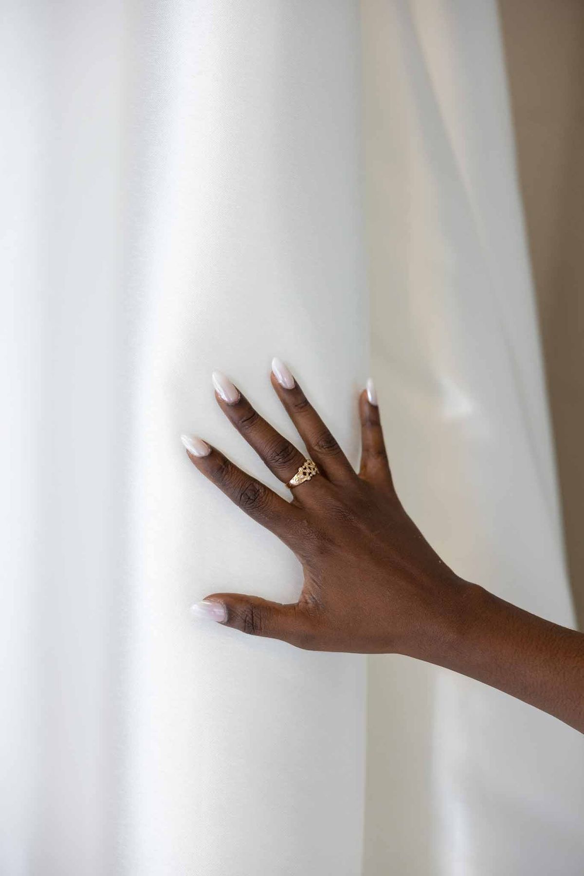 Bride's hand with gold ring against white satin wedding dress at Parc Mougins