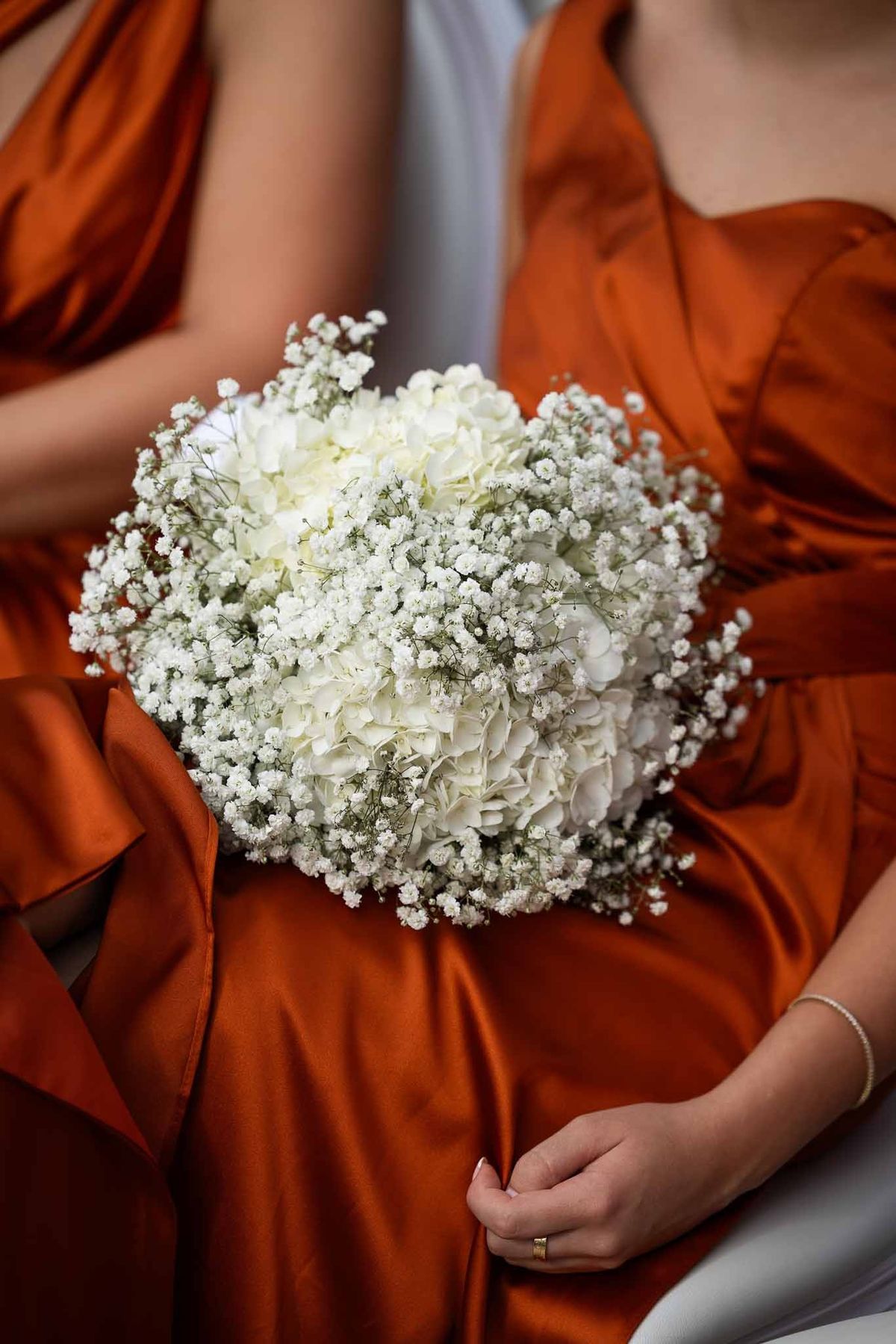 White hydrangea and baby's breath bouquet held by bridesmaids in burnt orange dresses