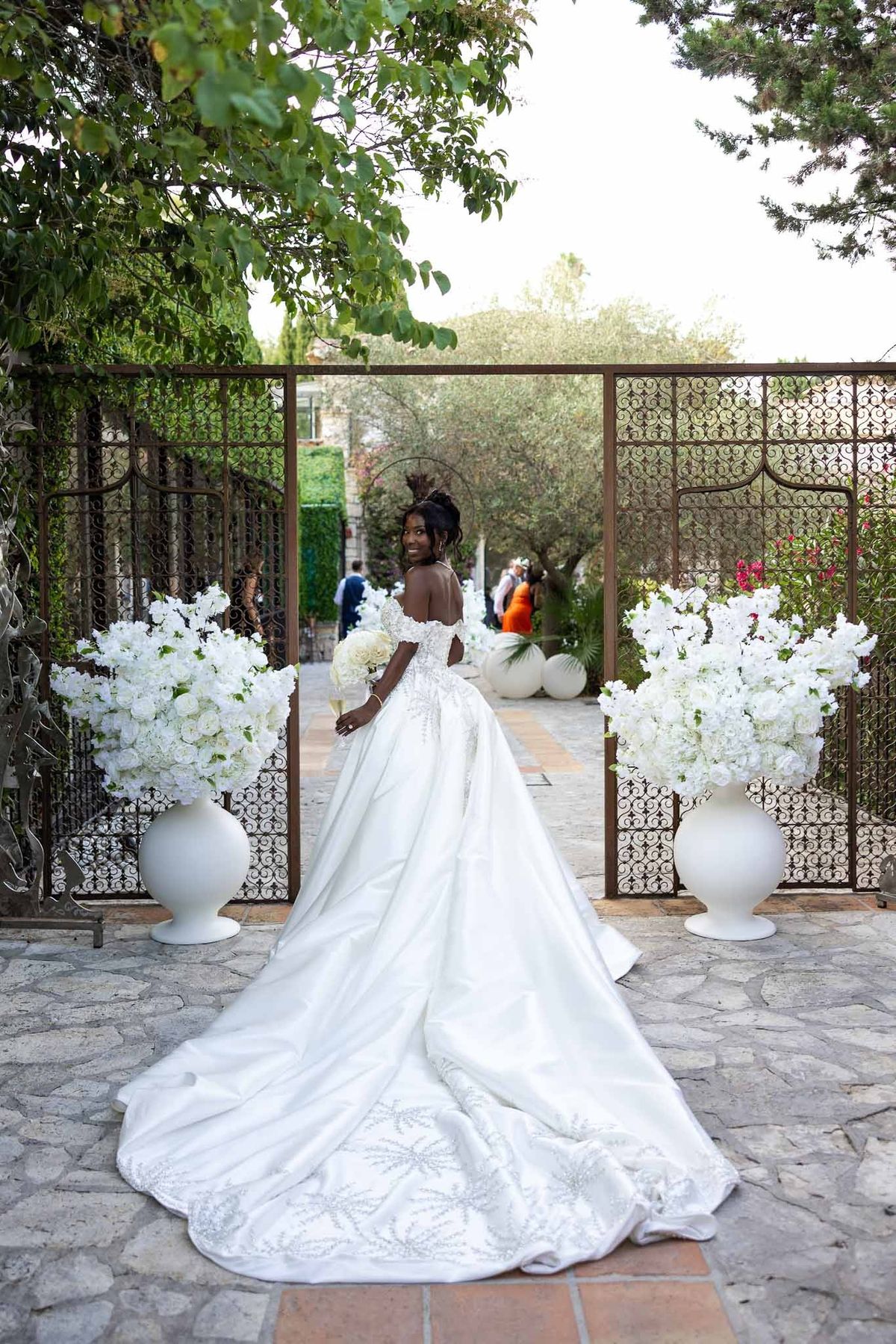 Bride in embroidered off-shoulder ball gown with long train at garden entrance at Parc Mougins