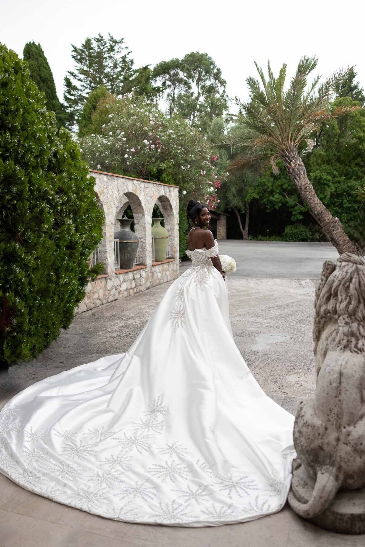 Bride in embroidered ball gown looking over shoulder in garden at Parc Mougins