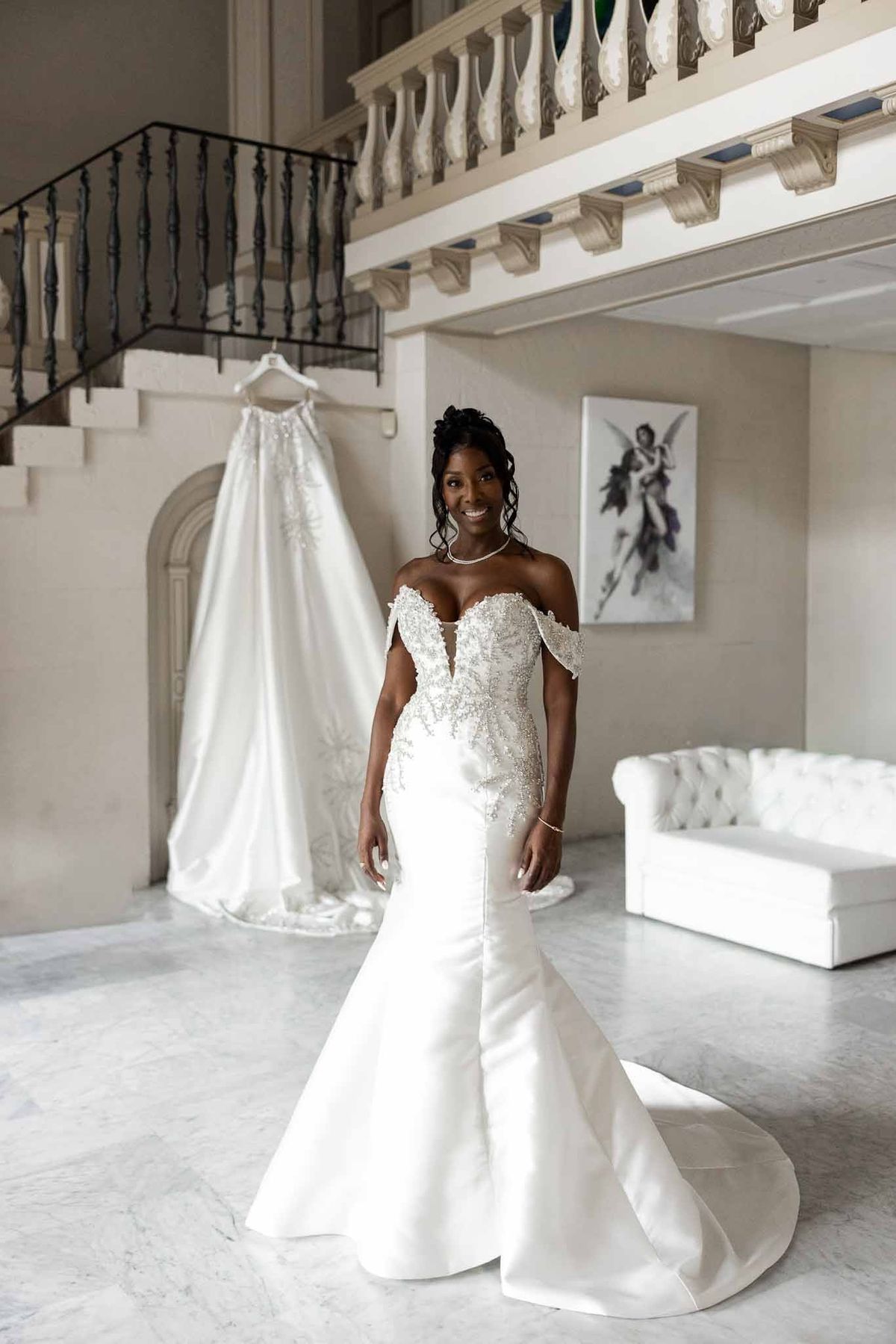 Bride in beaded mermaid dress with ball gown hanging behind her at Parc Mougins