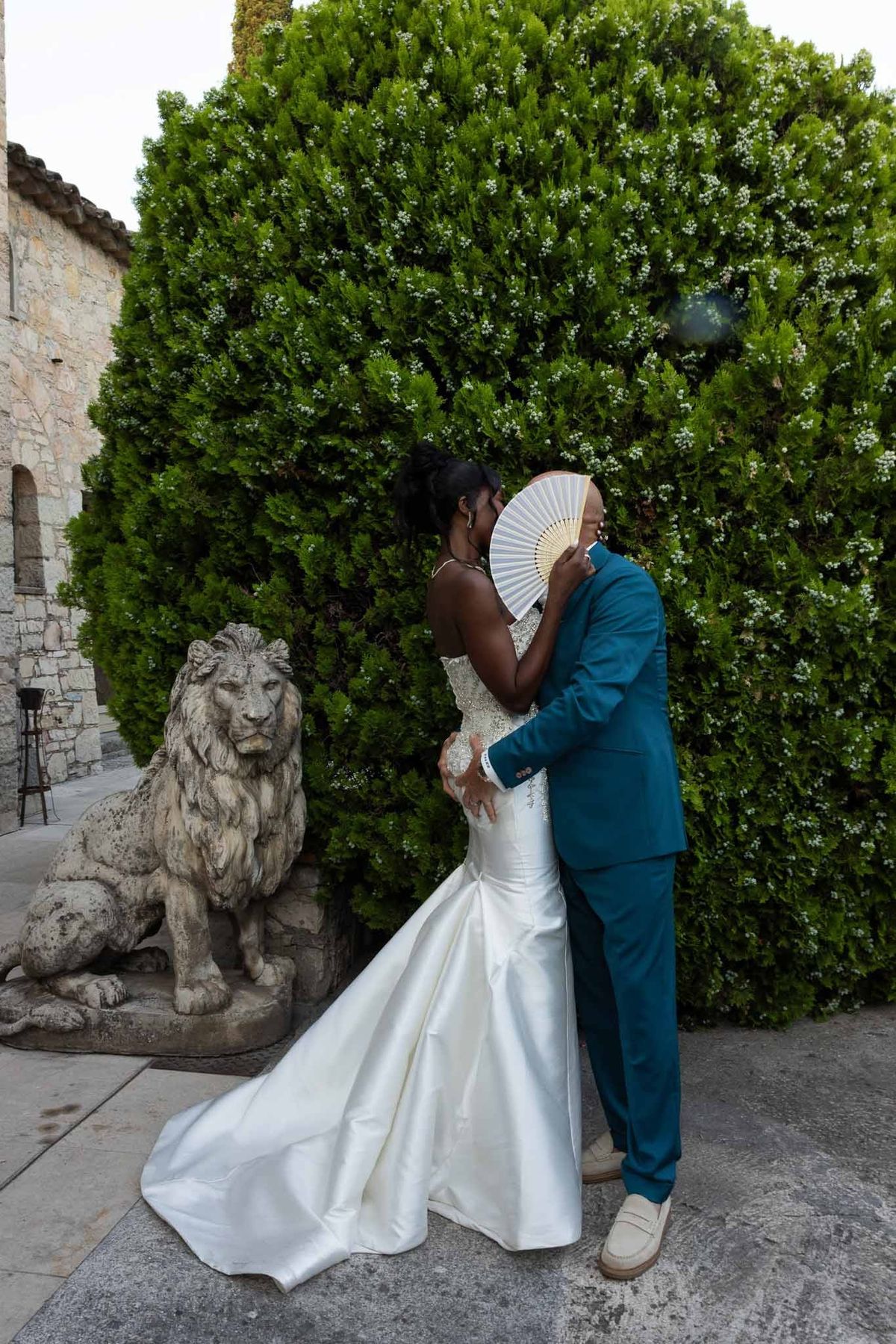 Bride and groom kissing beside lion statue in garden at Parc Mougins