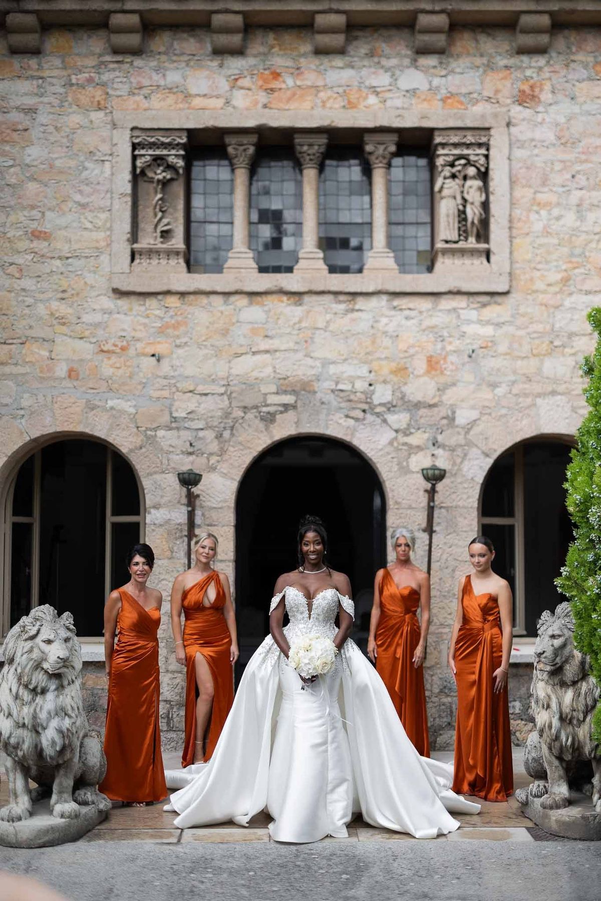 Bride and four bridesmaids in burnt orange dresses in front of stone façade at Parc Mougins