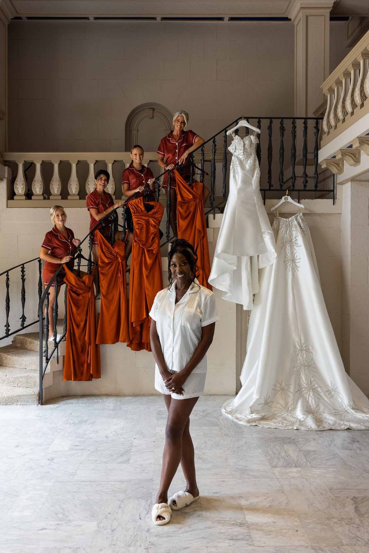 Bride and bridesmaids on marble staircase with dresses hanging at Parc Mougins