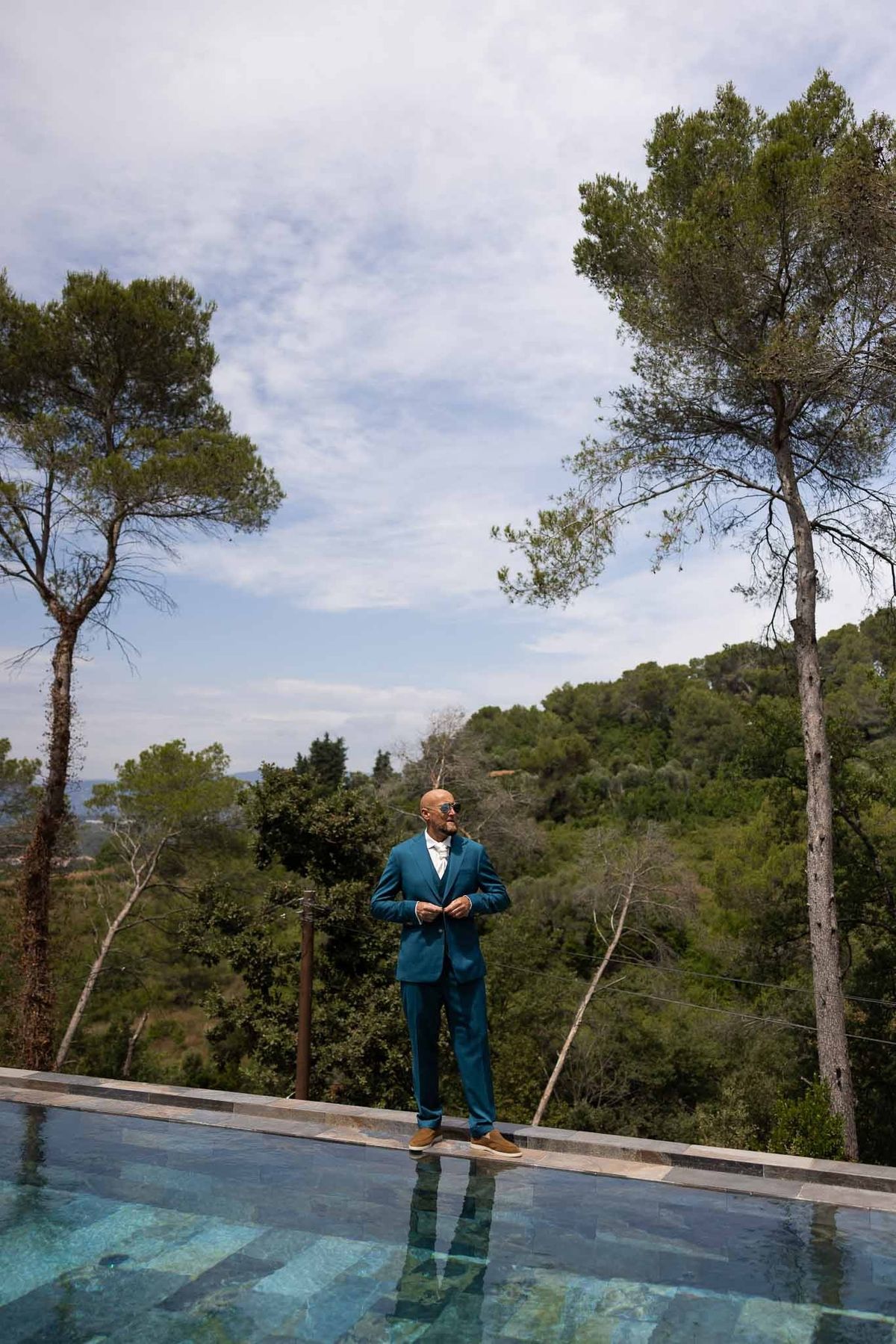 Groom in teal suit standing by infinity pool with Mediterranean views at Parc Mougins