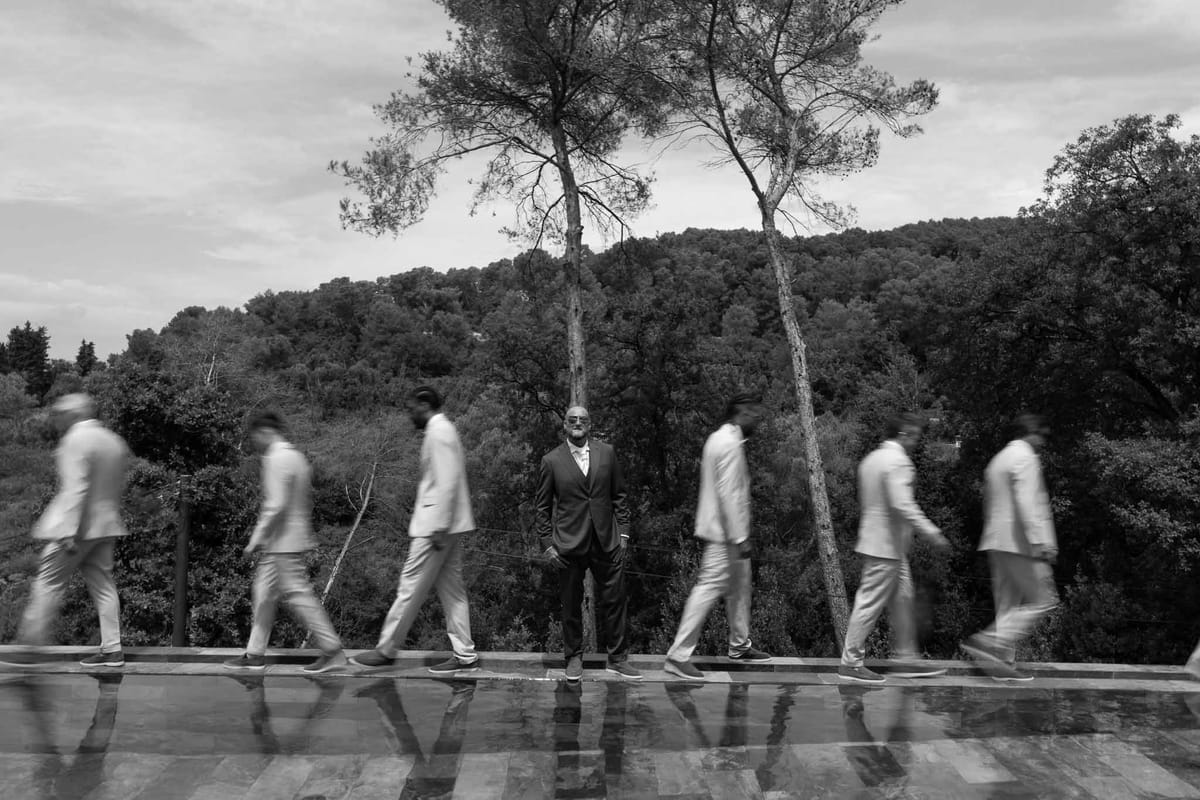 Groom standing still while groomsmen walk past in motion blur by pool at Parc Mougins