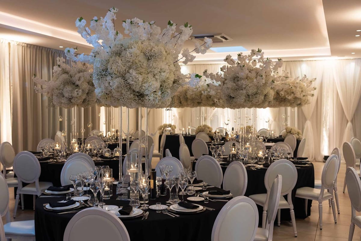 Reception room with black tables, white chairs and towering floral centrepieces at Parc Mougins