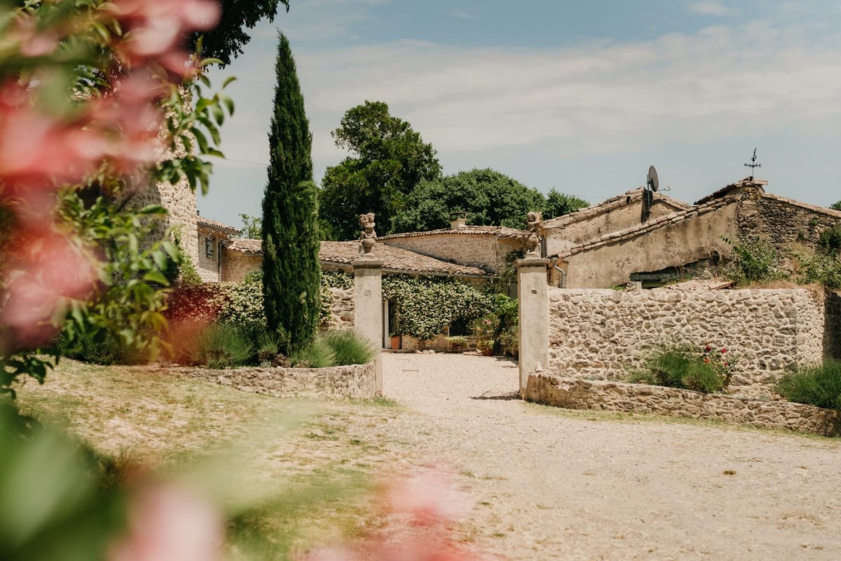 Stone farmhouse entrance with cypress tree and pink garden florals in Occitanie.