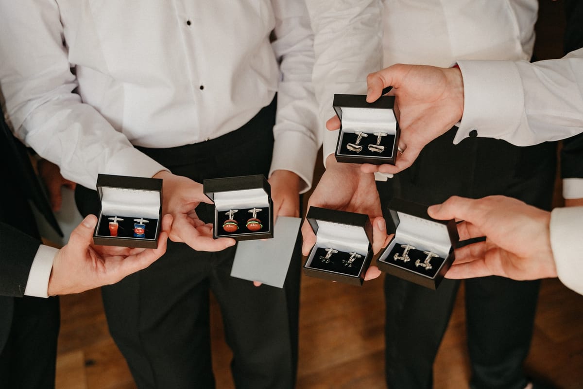 Five hands hold open boxes of cufflinks as groomsmen gifts in a getting ready moment.