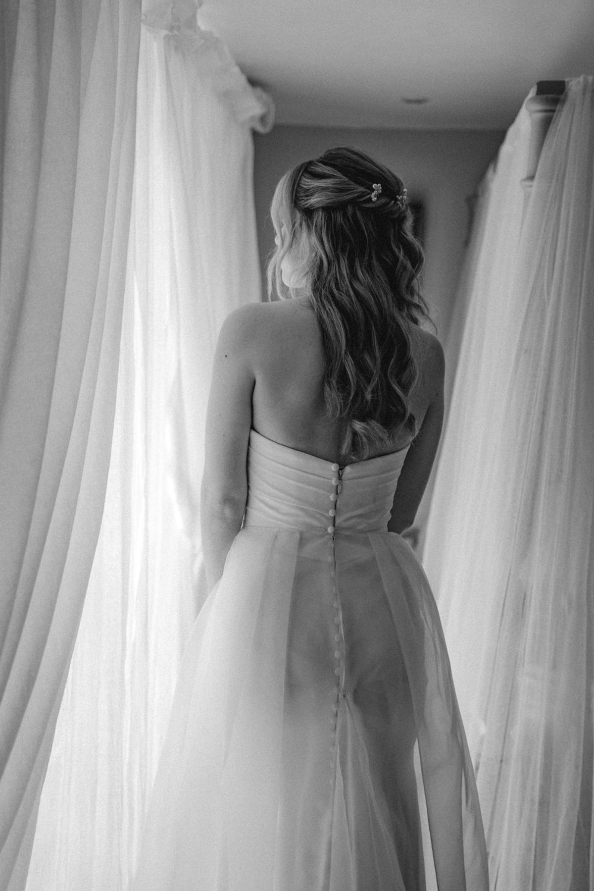 Black and white back view of bride in strapless gown with button detail and tulle overlay.