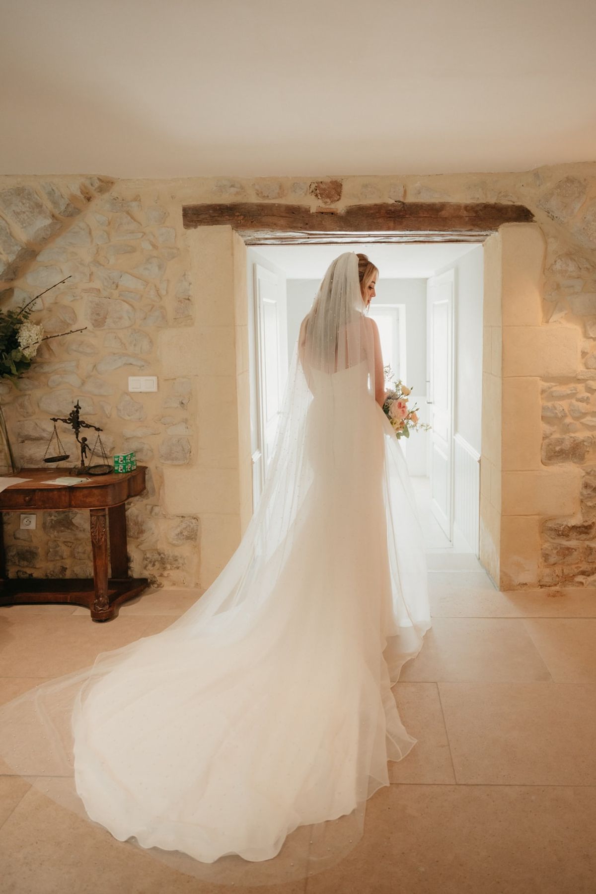 Bride in stone hallway with cathedral veil and tulle overlay train fanned across limestone floor.