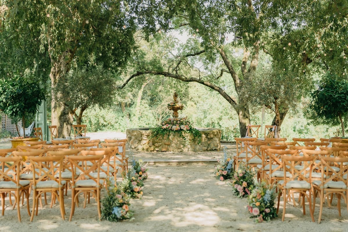 Empty ceremony space with stone fountain altar in pastel florals and crossback chair aisle.