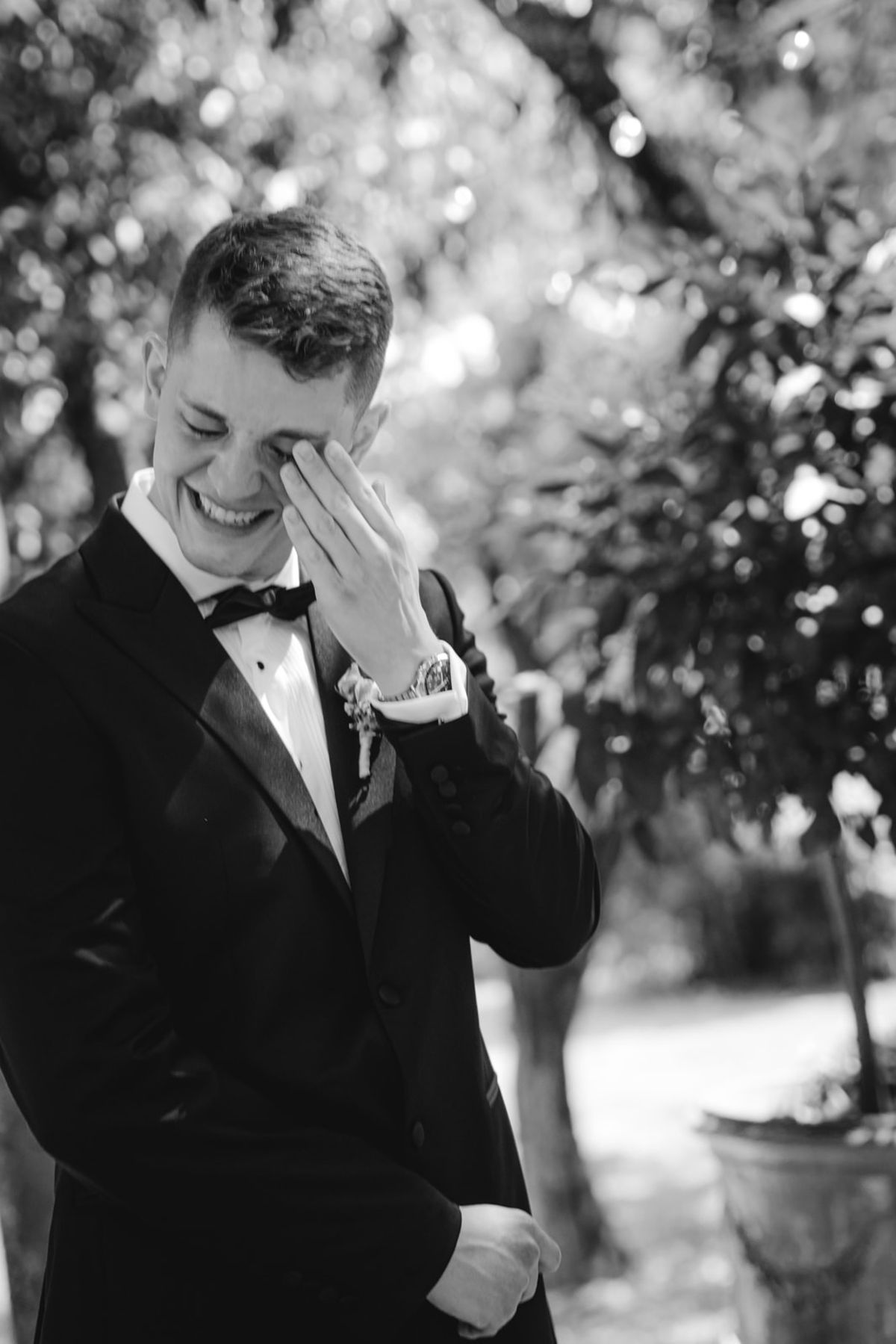 Black and white groom laughing and wiping his eye outside the ceremony in a tuxedo.