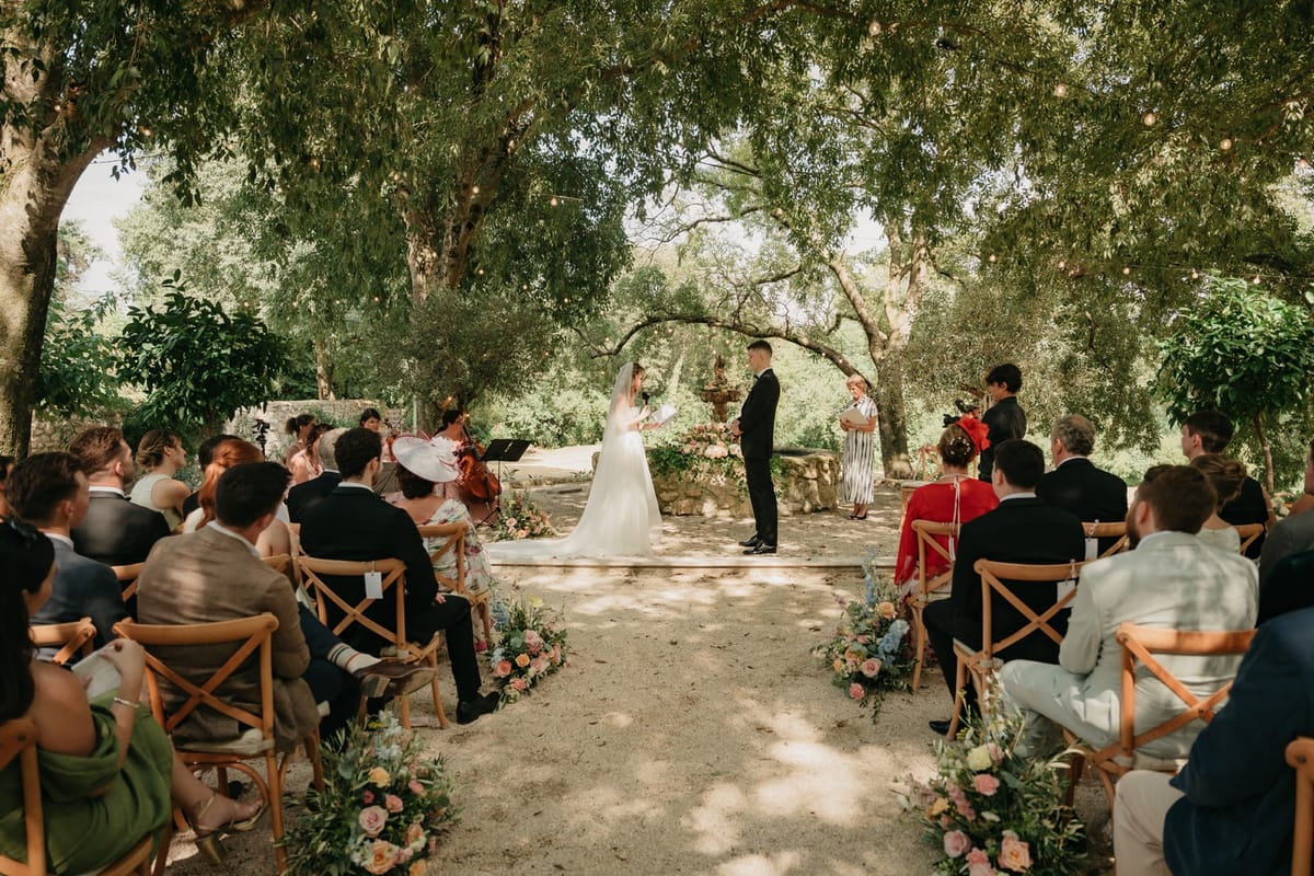 Wide ceremony view with couple at fountain altar, cellist in foreground and seated guests.