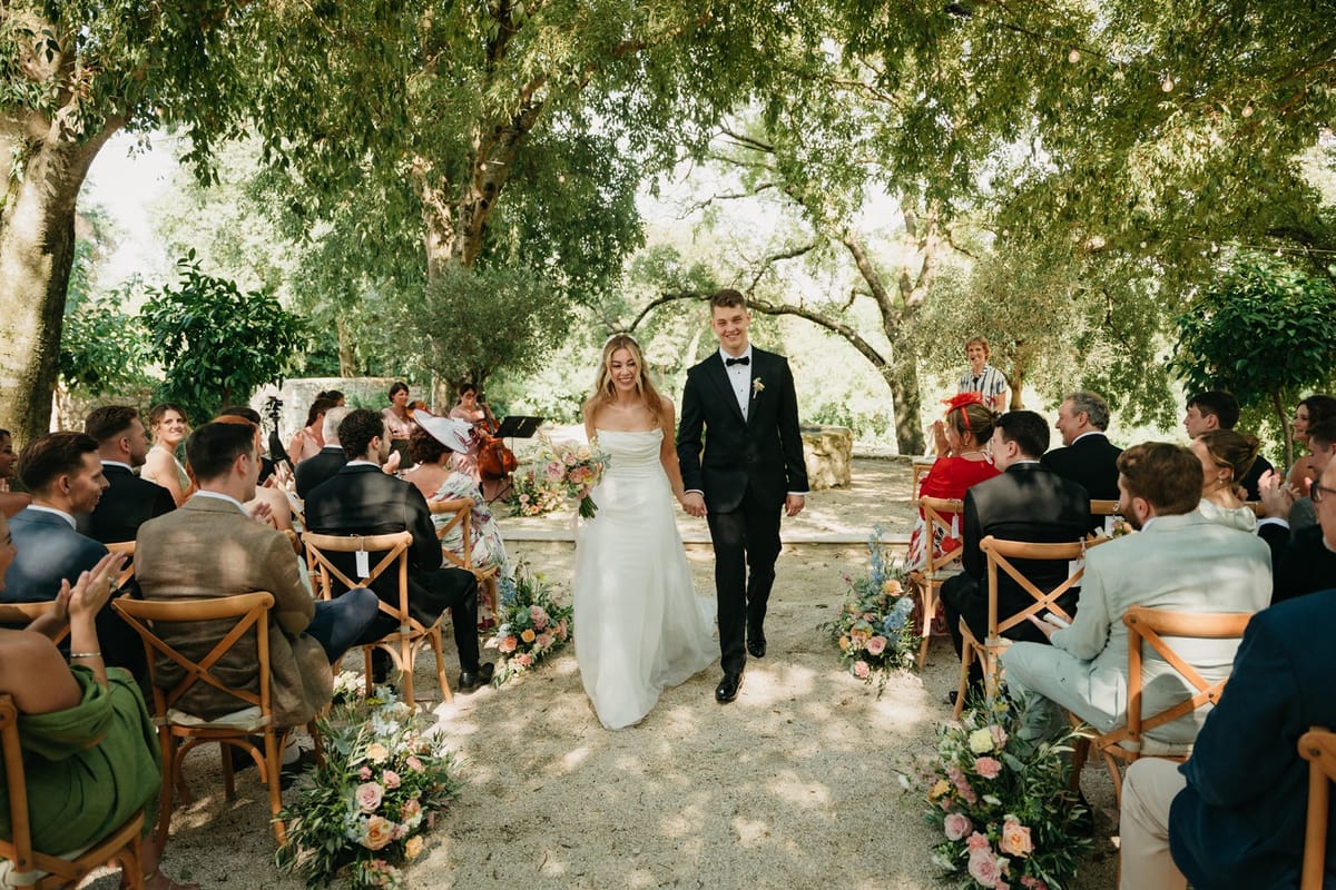 Newlyweds walk hand in hand down the aisle as guests rise to cheer on either side.