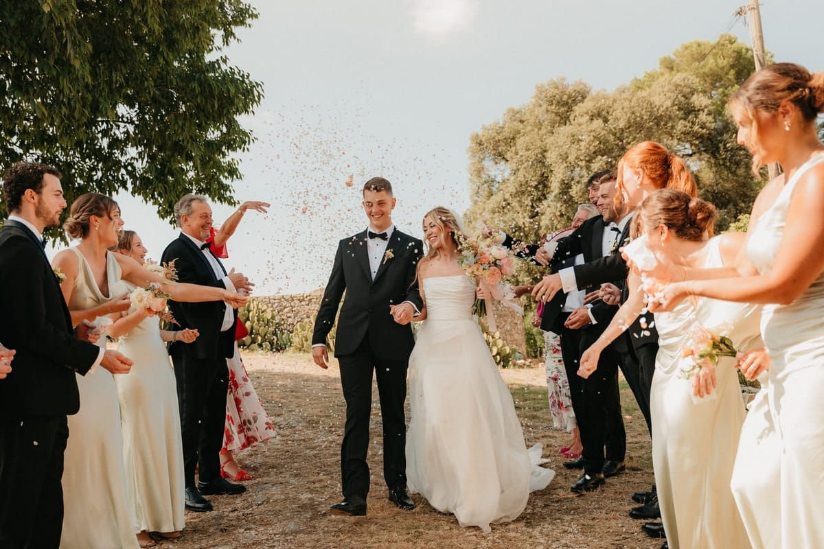 Newlyweds walk through confetti petal shower as guests toss handfuls on either side.