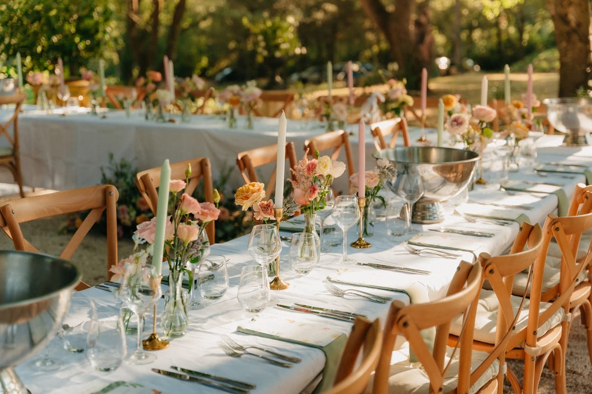 Open-air long banquet tables with sage and blush tapers, bud-vase florals and silver coolers.