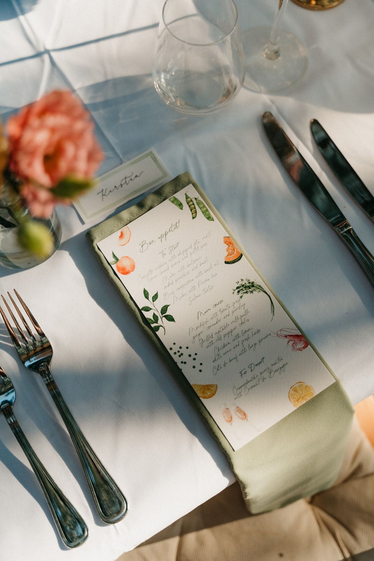 Place setting close-up with sage napkin, illustrated menu card and blush garden rose bud vase.