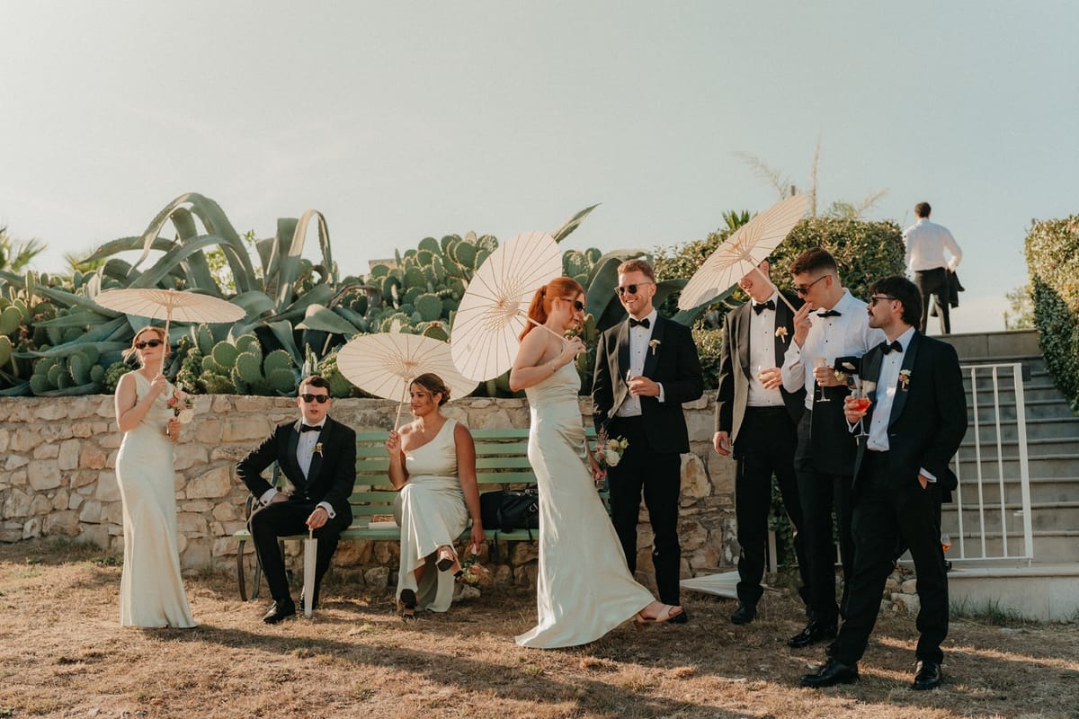Guests with cocktails on terrace beside cactus garden, several holding paper parasols.