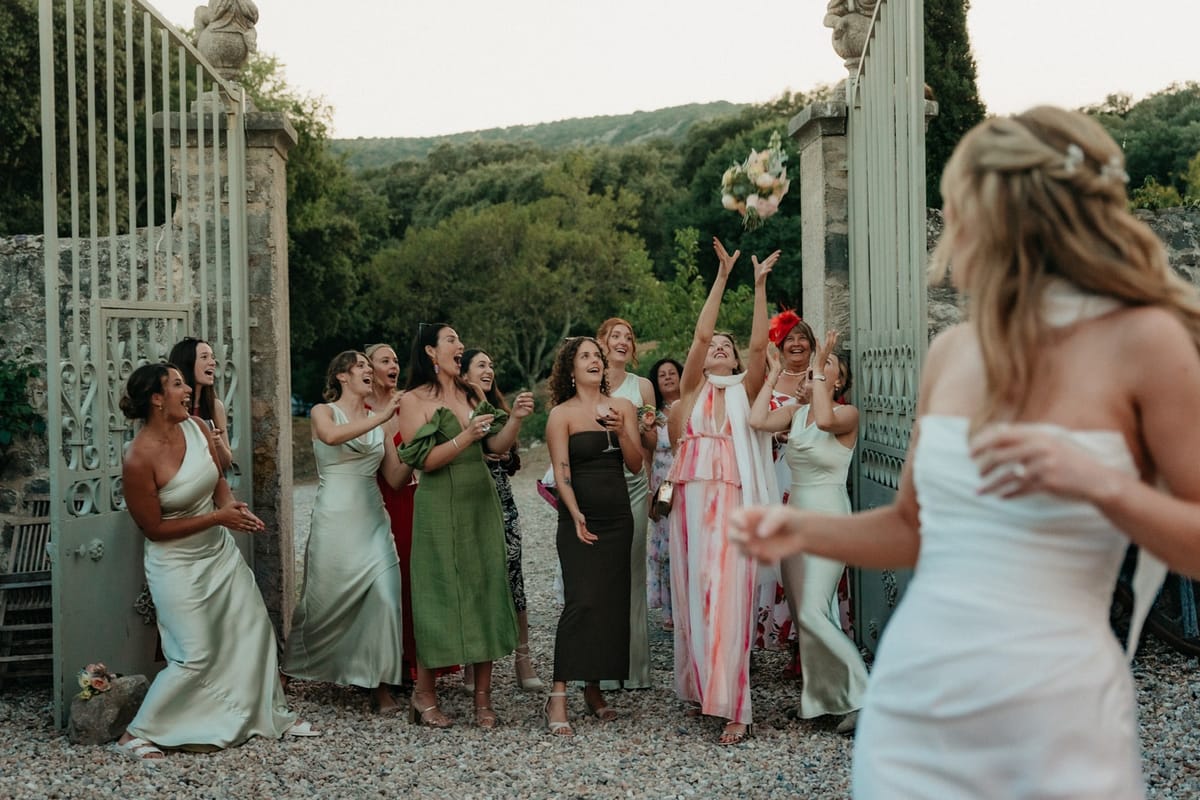 Wide bouquet toss frame with women guests reaching as one in pink jumps for the bouquet.