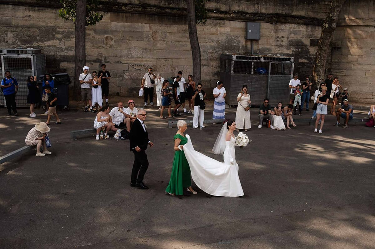 Bride in ballgown with cathedral veil escorted across Paris plaza as 20 onlookers watch and photograph