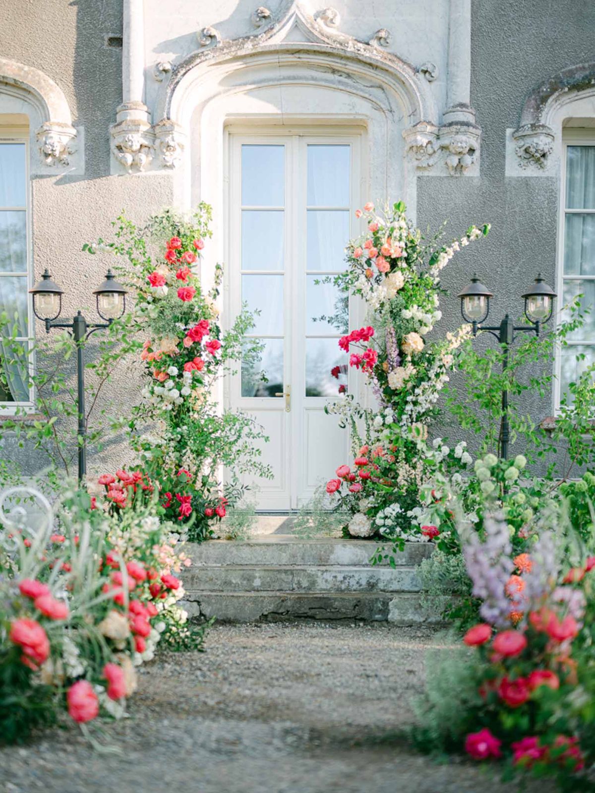 Floral column entrance installation with coral, pink, and white blooms flanking chateau doors