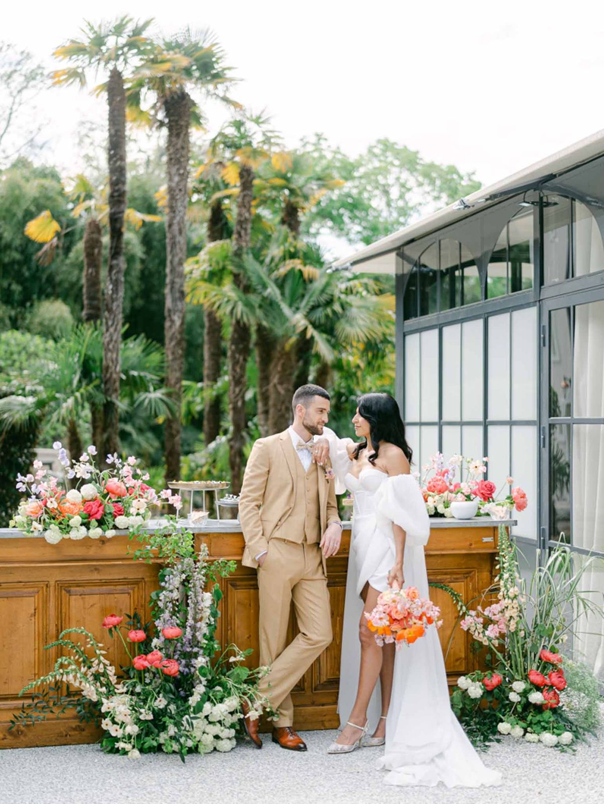 Bride and groom at wooden bar decorated with coral ranunculus and lavender delphinium arrangements