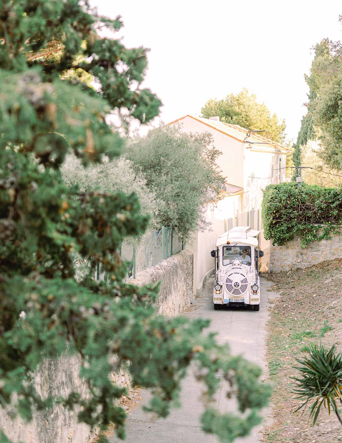 White petit train guest shuttle approaching along stone-walled lane at southern French estate