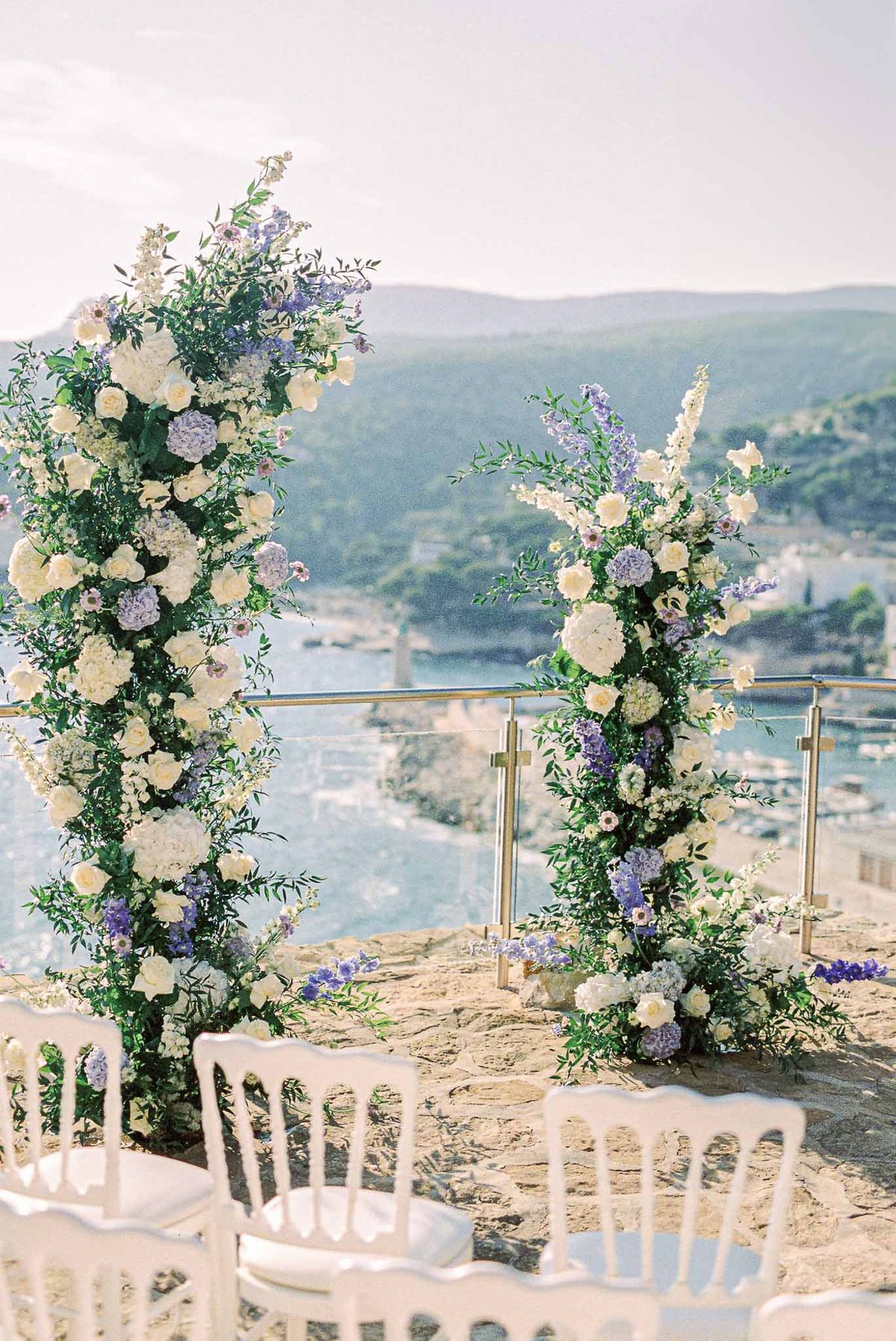 Coastal ceremony terrace with tall floral column arch of ivory roses and lavender hydrangeas