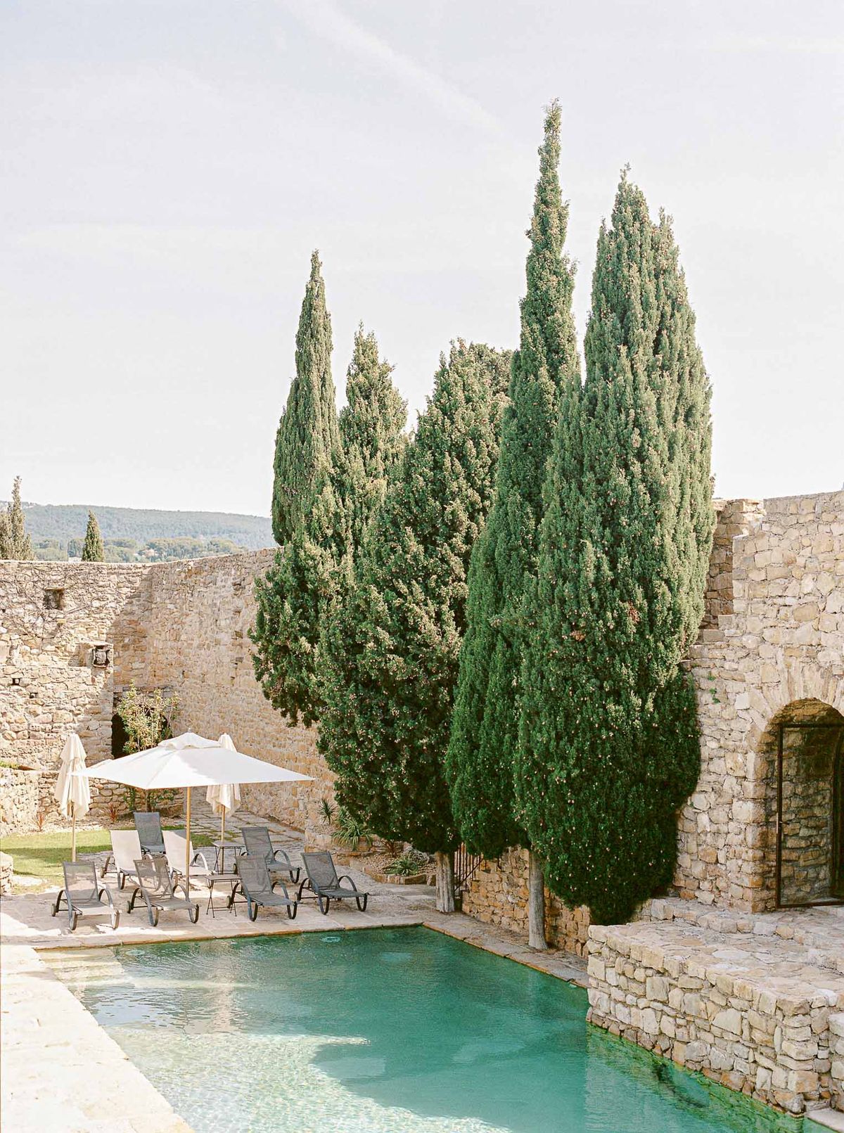 Rectangular pool with turquoise water flanked by sun loungers and cypress trees at Provencal stone venue