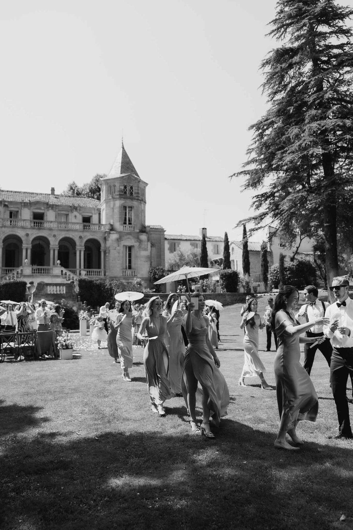 Black and white bridesmaids in satin dresses walking across chateau lawn with turret behind