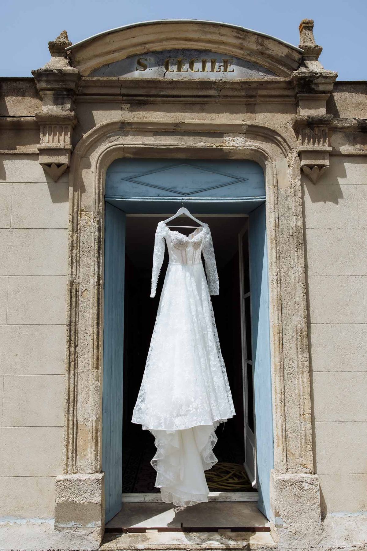 White lace gown with long sleeves hanging in carved limestone doorway inscribed S. Cecile with pale blue doors