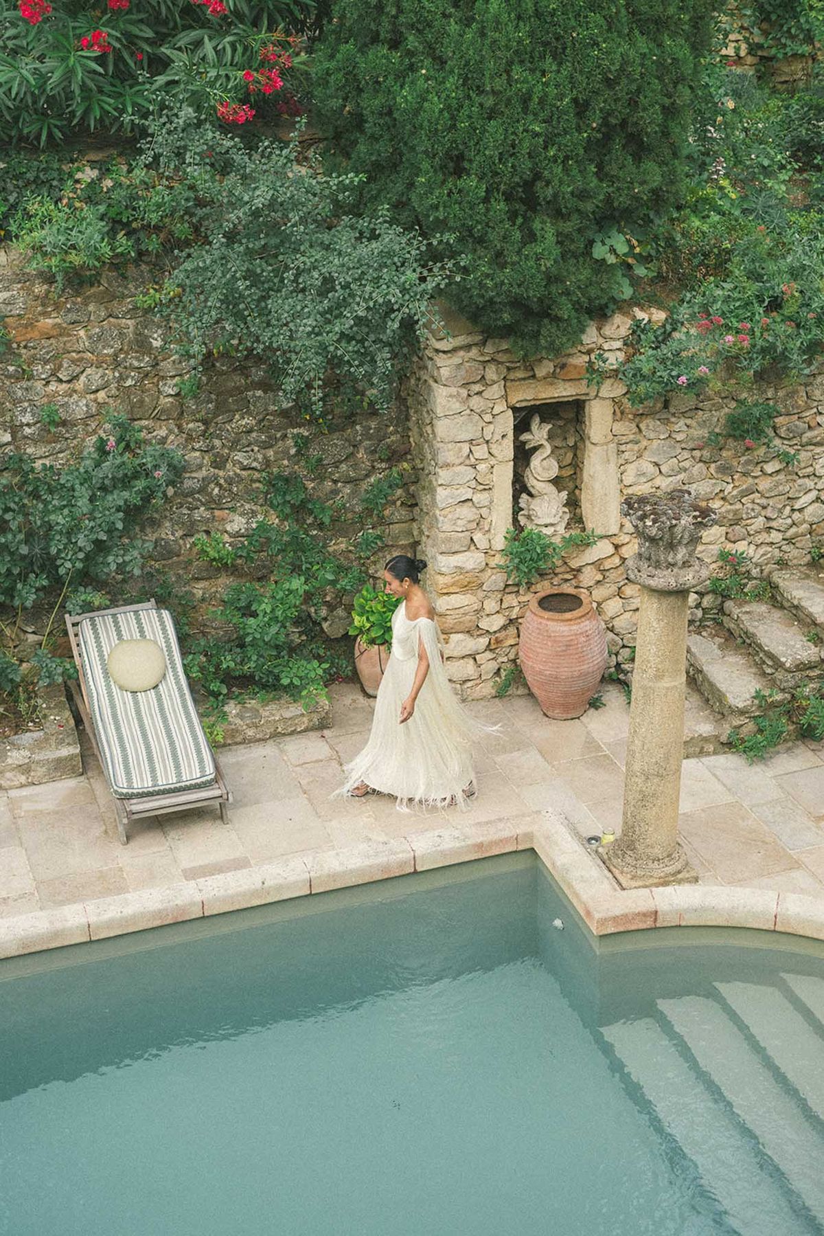 Bride in flowing off-white fringed dress walking along stone poolside terrace at a Provencal property