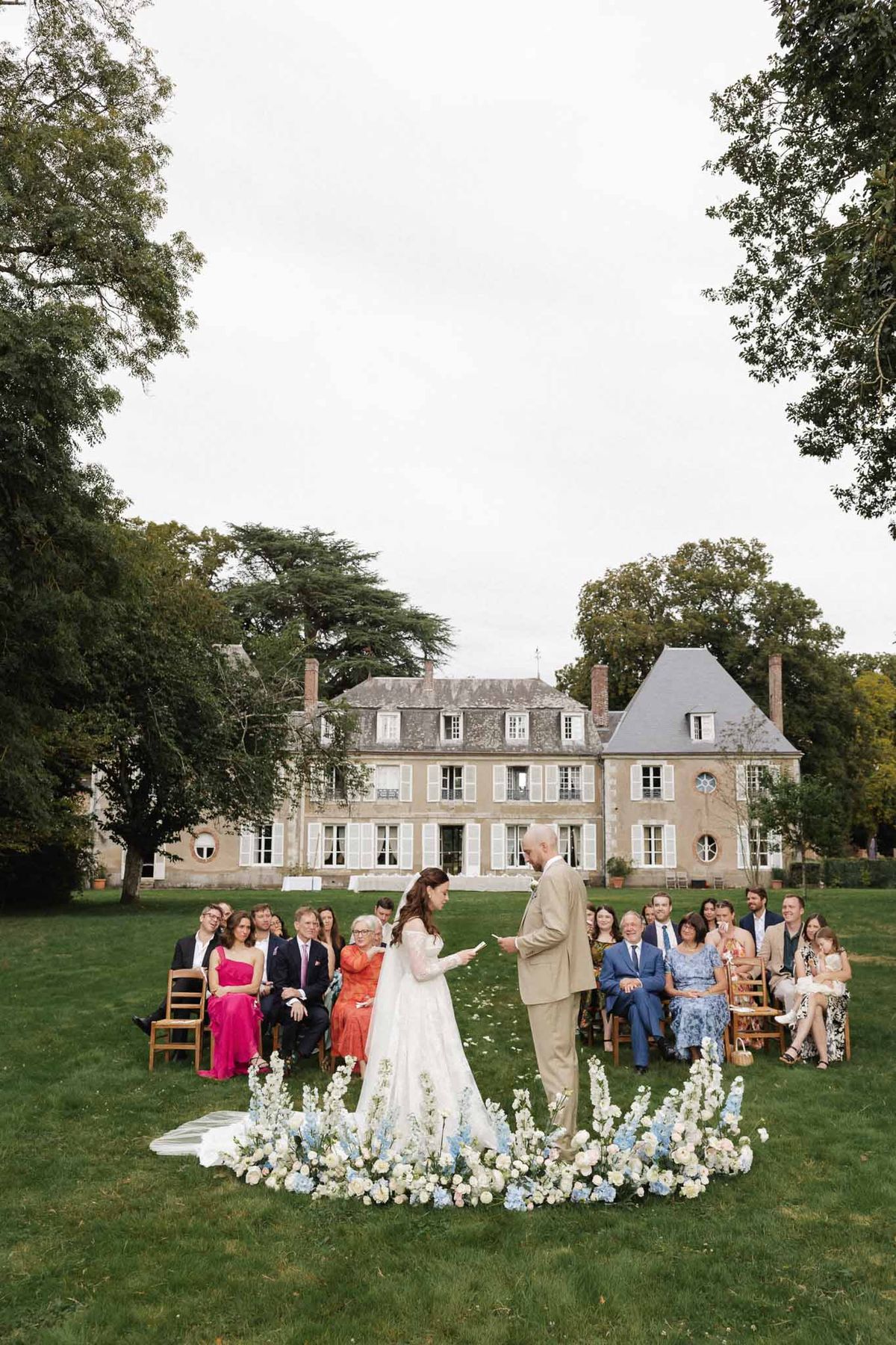Bride reads vows to groom at curved white and blue hydrangea altar with 30 guests before chateau
