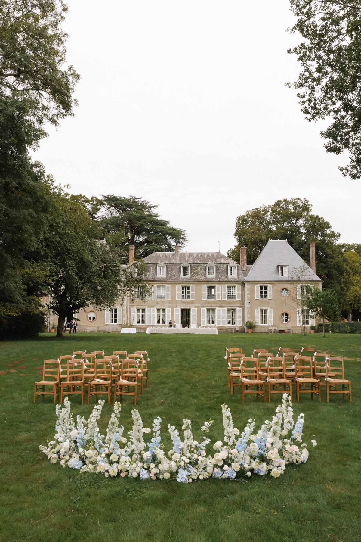 Ceremony setup with white and blue delphiniums and blush roses on chateau lawn with turret behind