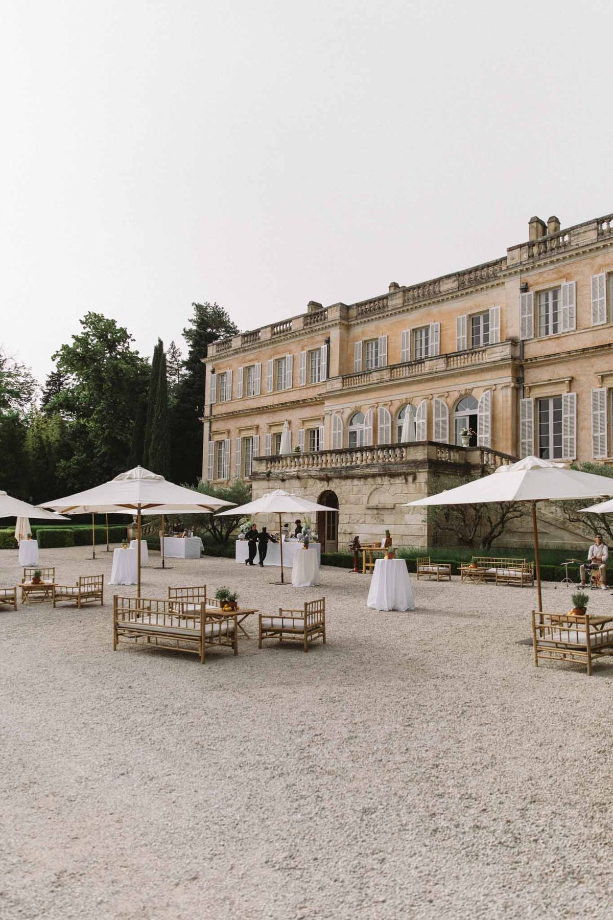 Cocktail hour setup with rattan seating and white umbrellas on chateau courtyard forecourt