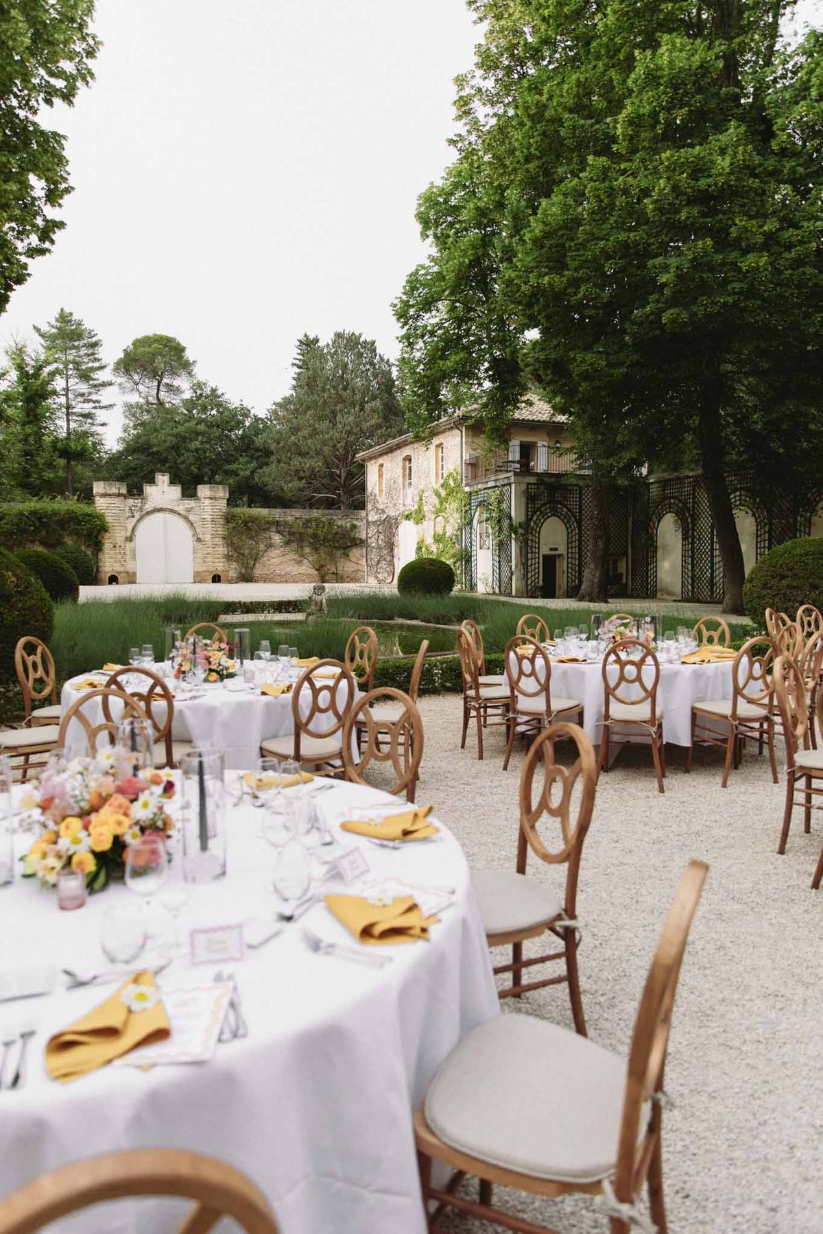 Outdoor wedding reception tables with yellow napkins and mixed floral centerpieces on a gravel terrace at a French estate