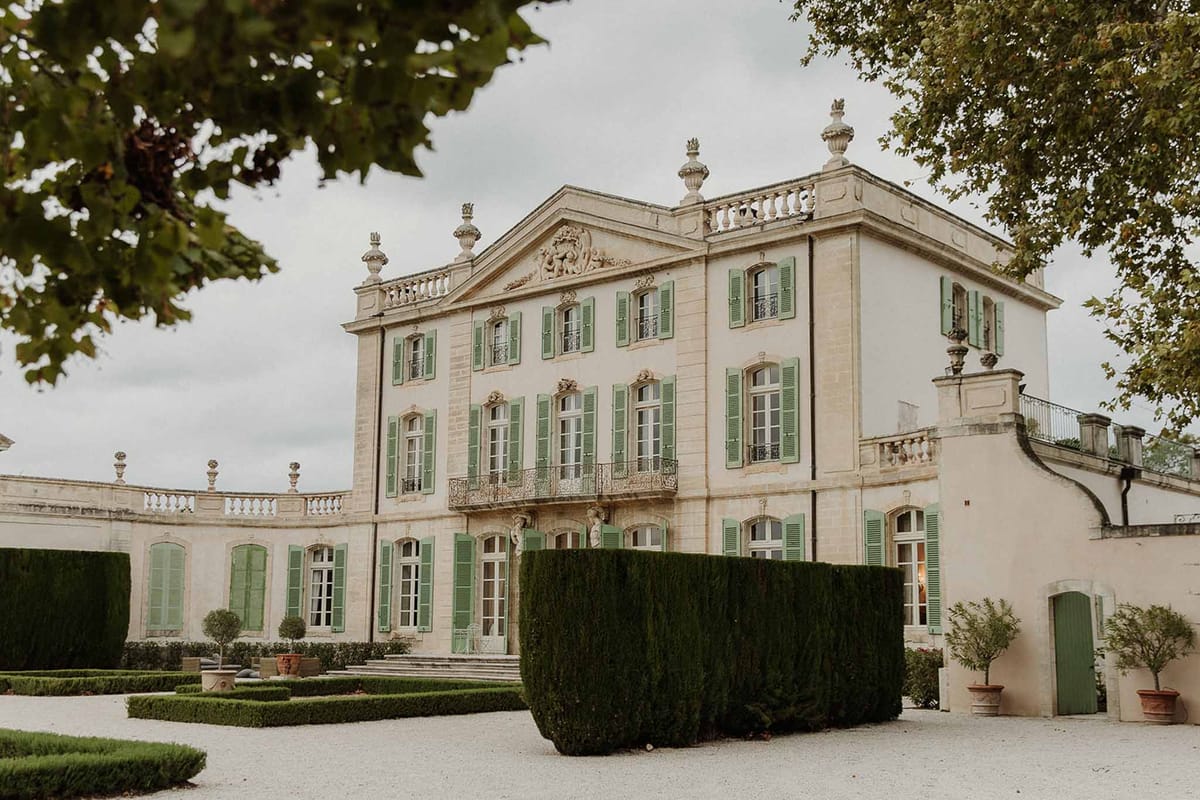 Three-storey cream chateau with sage shutters stone pediment iron balconies and geometric box hedging
