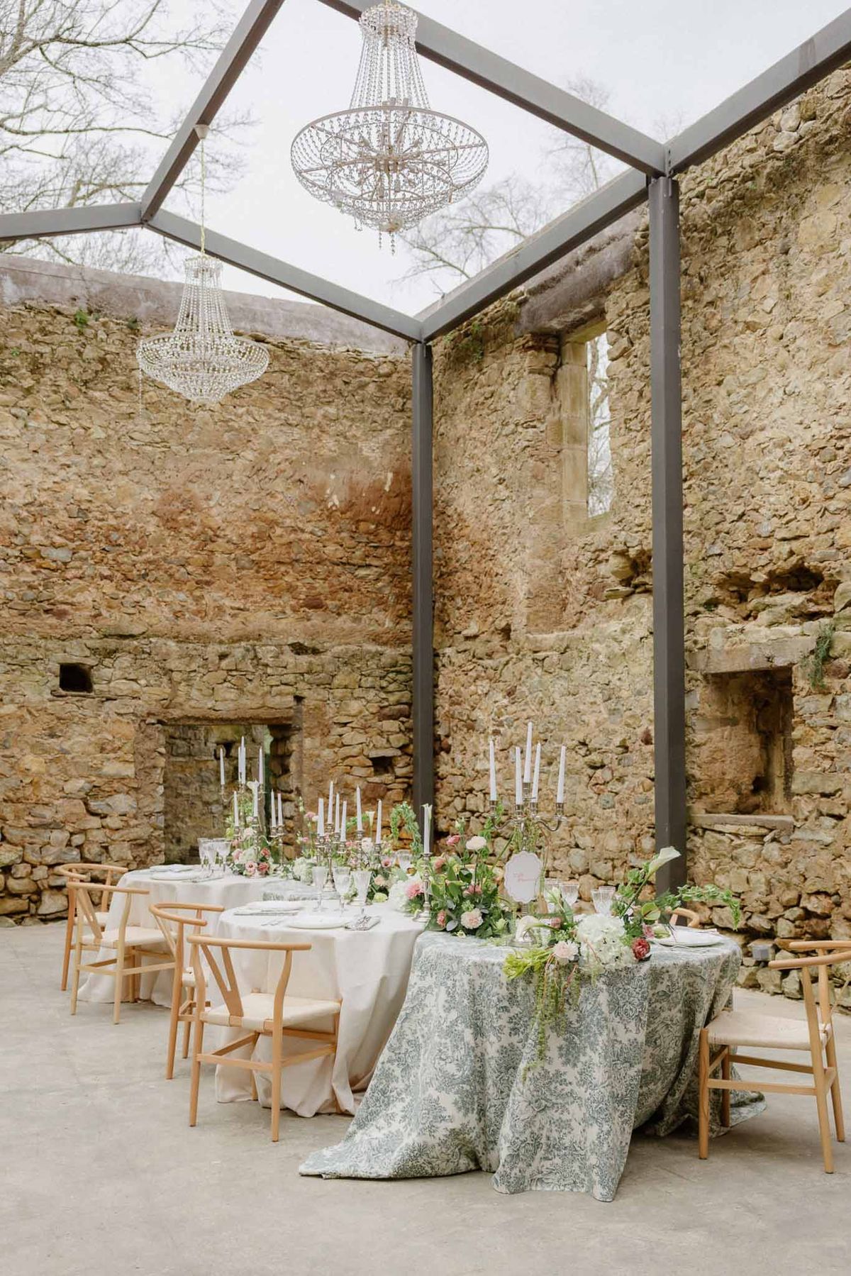 Long reception table in glass-roofed stone ruin with crystal chandeliers, silver candelabras, and blush florals