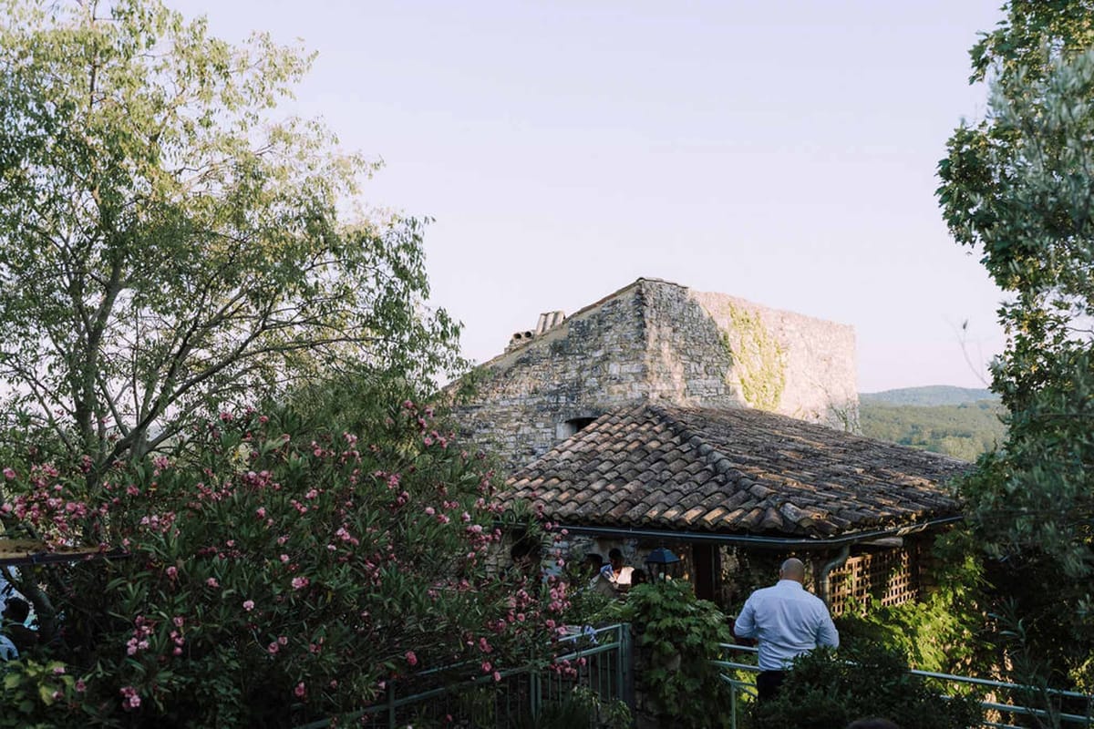 Guests gathered on a terrace at a rustic stone venue with ancient tower and pink oleander bushes
