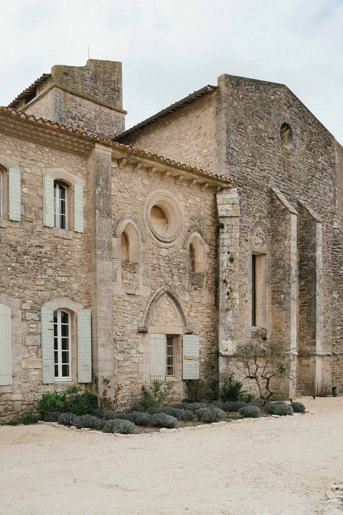 Romanesque stone abbey with rose window, Gothic arched doors, sage shutters, and lavender-bordered gravel courtyard