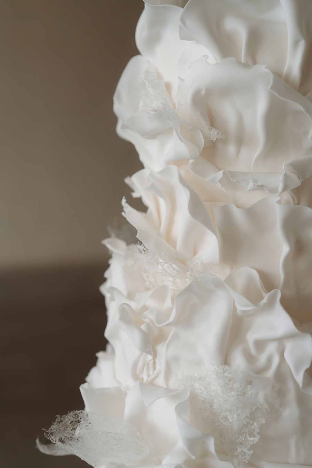 Multi-tier wedding cake decorated with layered ivory and white fondant ruffles and sugar crystal accents